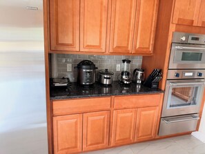 Una cocina con armarios de madera, una estufa de acero inoxidable y varios electrodomésticos, incluyendo una licuadora y una olla de cocción lenta.
