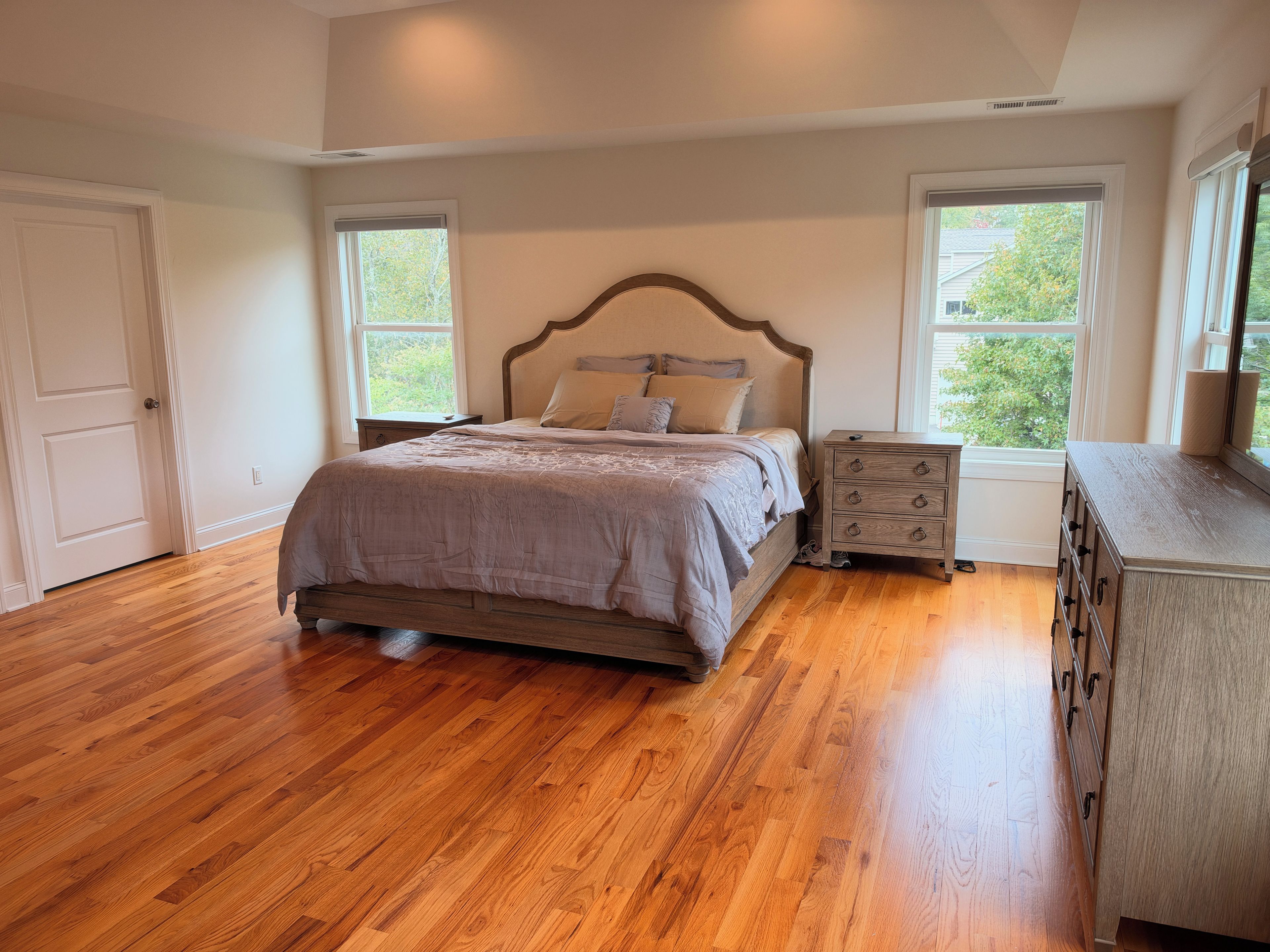 A bedroom with a wooden floor, a bed with a headboard, a nightstand, and a dresser.