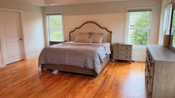 A bedroom with a wooden floor, a bed with a headboard, a nightstand, and a dresser.