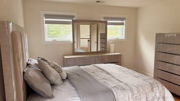 A bedroom with a bed, a dresser, a mirror, and two windows.