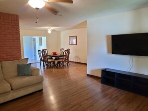 A living room with a sofa, dining table, chairs, a flat-screen TV, and a brick accent wall. - Fall Escape at Spanish Style 4br/3ba home! (Niceville)