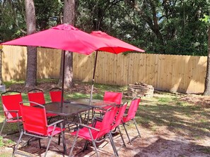 An outdoor patio with a table and chairs, a red umbrella, and a wooden fence in the background. - Fall Escape at Spanish Style 4br/3ba home! (Niceville)