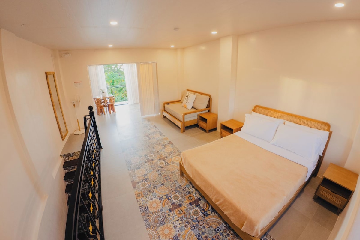 A bedroom with a large bed, a sitting area with a sofa, and a dining table.