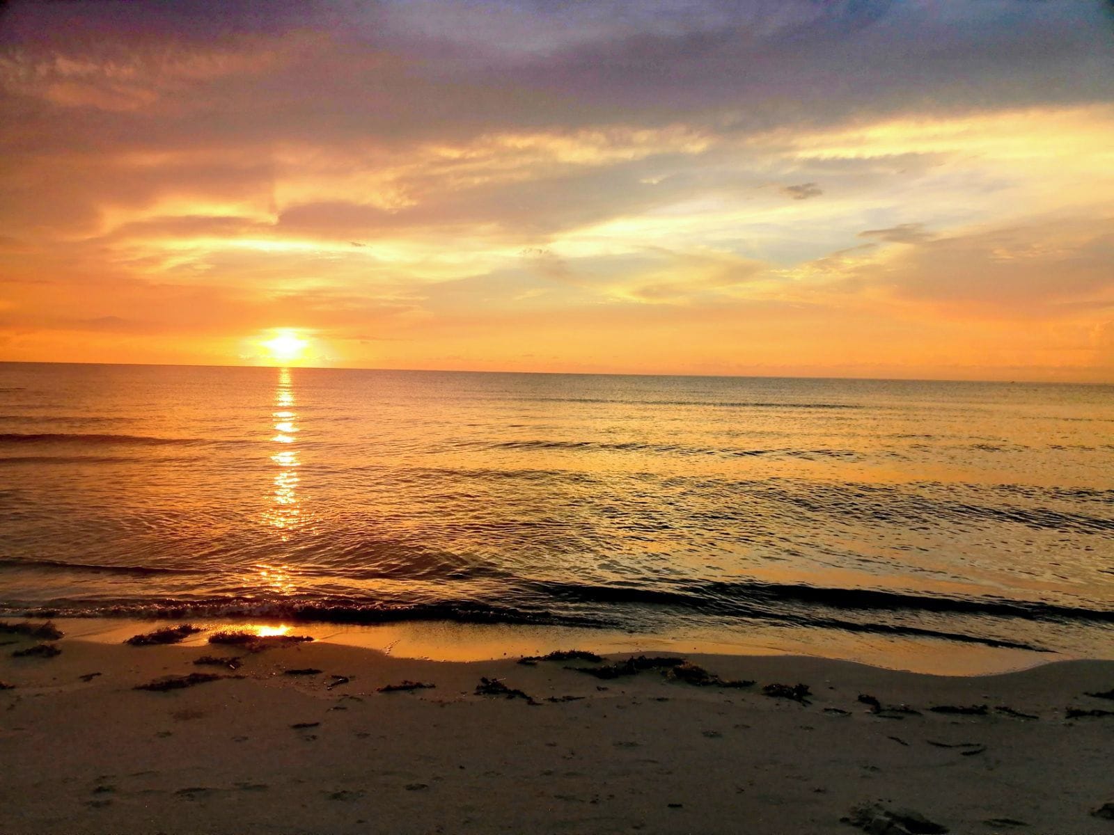 A beach with the sun reflecting on the water, creating a path of light on the sand.