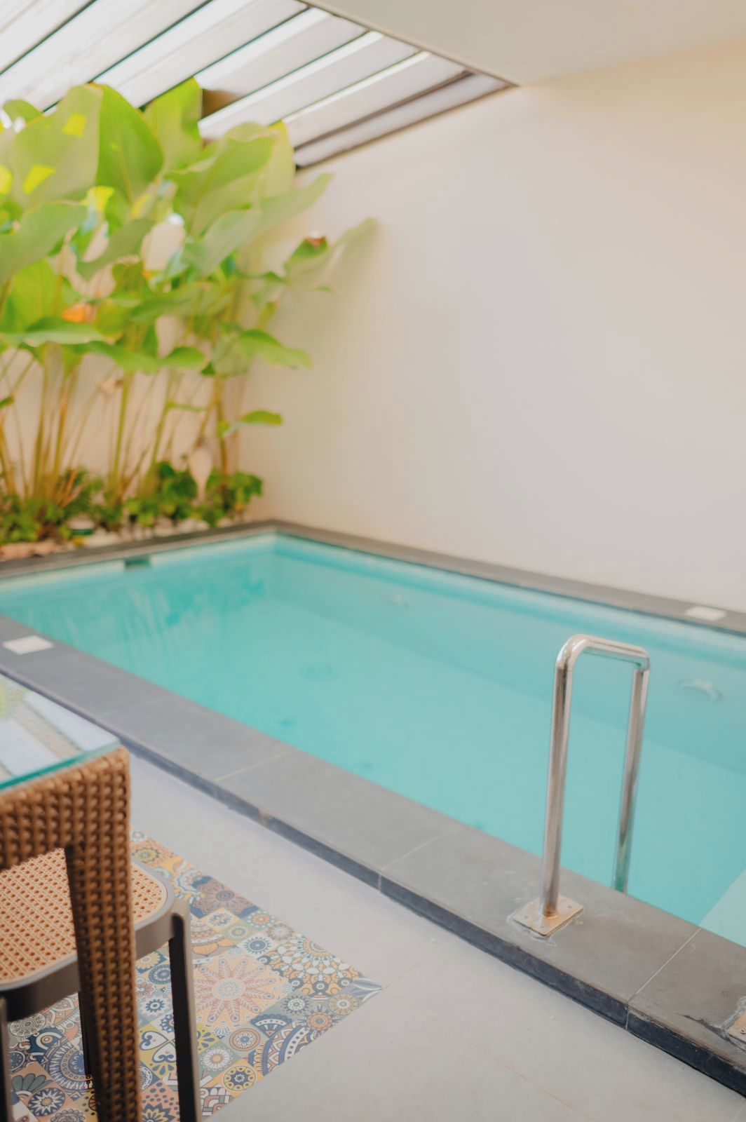 Uma piscina interior com vista clara da água, uma escada de metal e uma cadeira de vime.