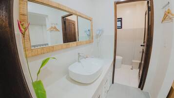 Un baño con un lavamanos blanco, un espejo grande y una puerta de madera que da a la zona de la ducha.