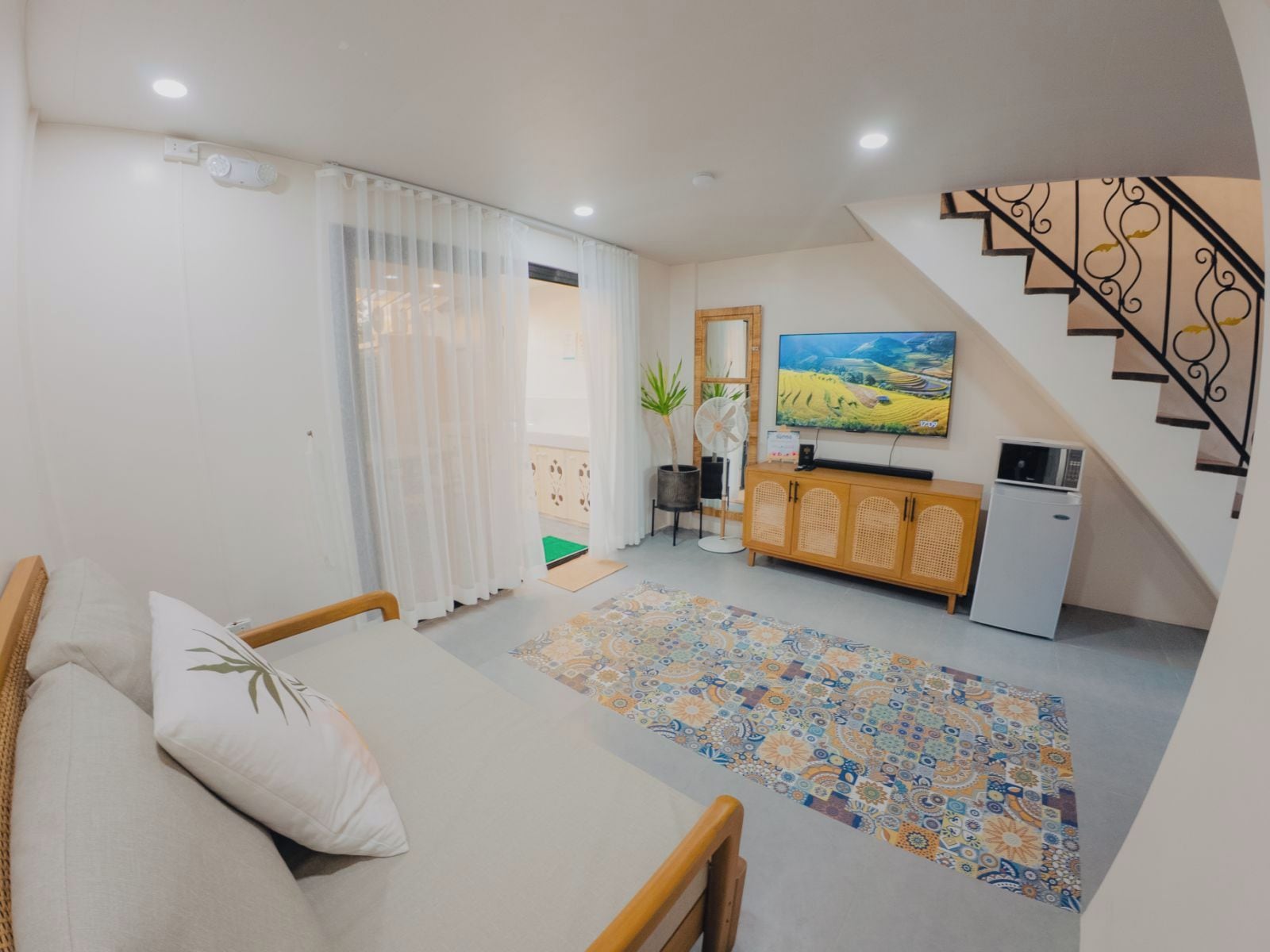 Un salon comprenant un canapé, un téléviseur, une petite kitchenette et un escalier.