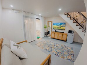 A living room with a sofa, a TV, a small kitchenette, and a staircase.