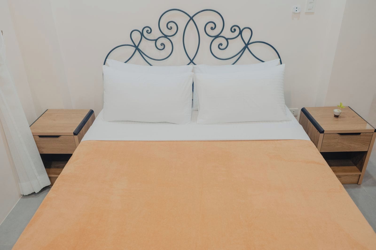 Una cama con cabecera de madera, dos mesitas de noche y un almohadón blanco.