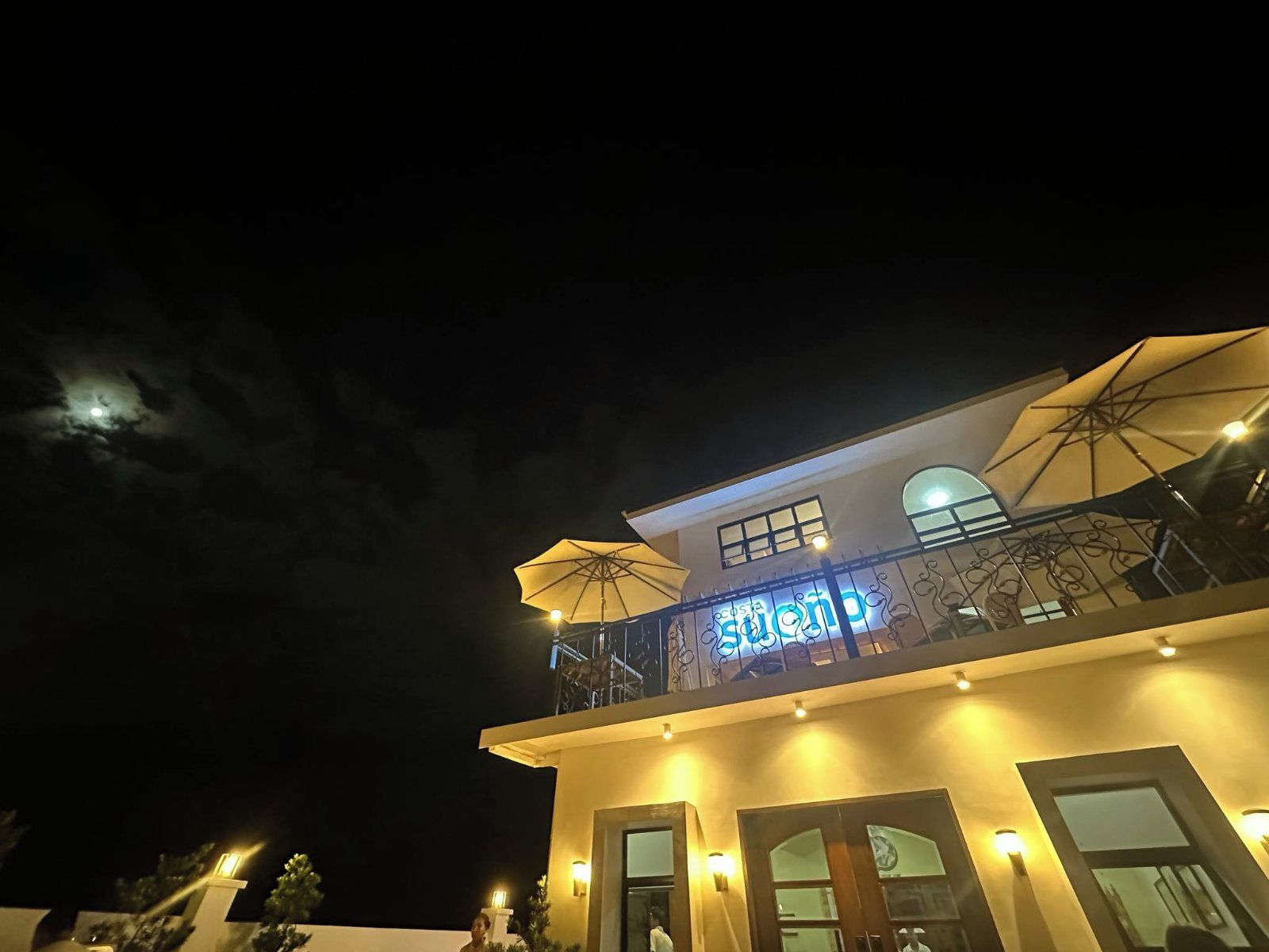 Um edifício com varanda, um guarda-sol grande e um letreiro com letras iluminadas.