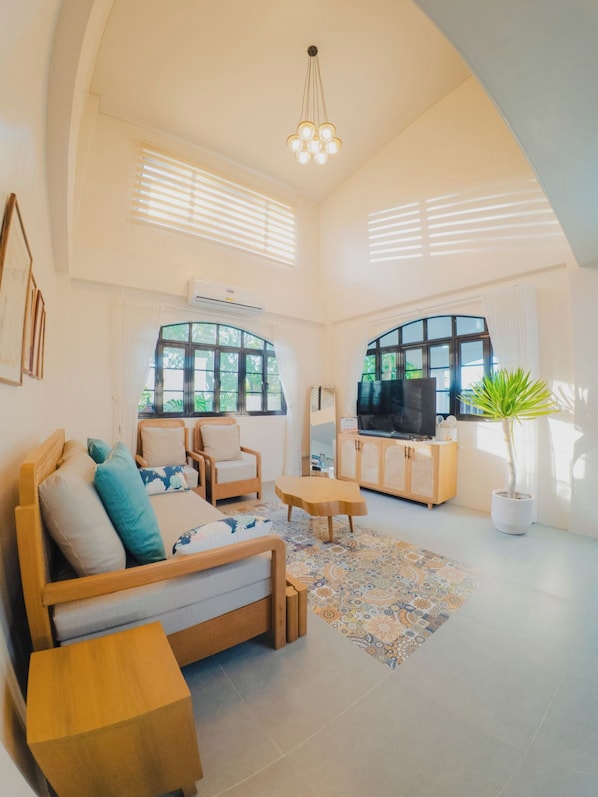 A spacious living room with a sofa, chairs, a TV, and a potted plant.