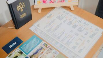 A wooden table with a welcome sign, a Holy Bible, a menu, and a remote control.