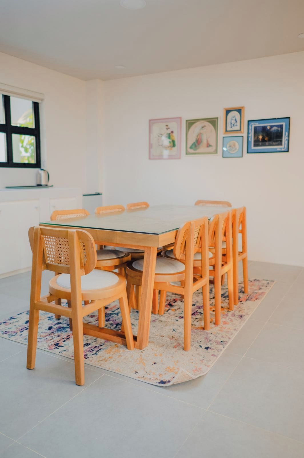 Un comedor con una mesa redonda y seis sillas, un tapete estampado y cuadros en la pared.
