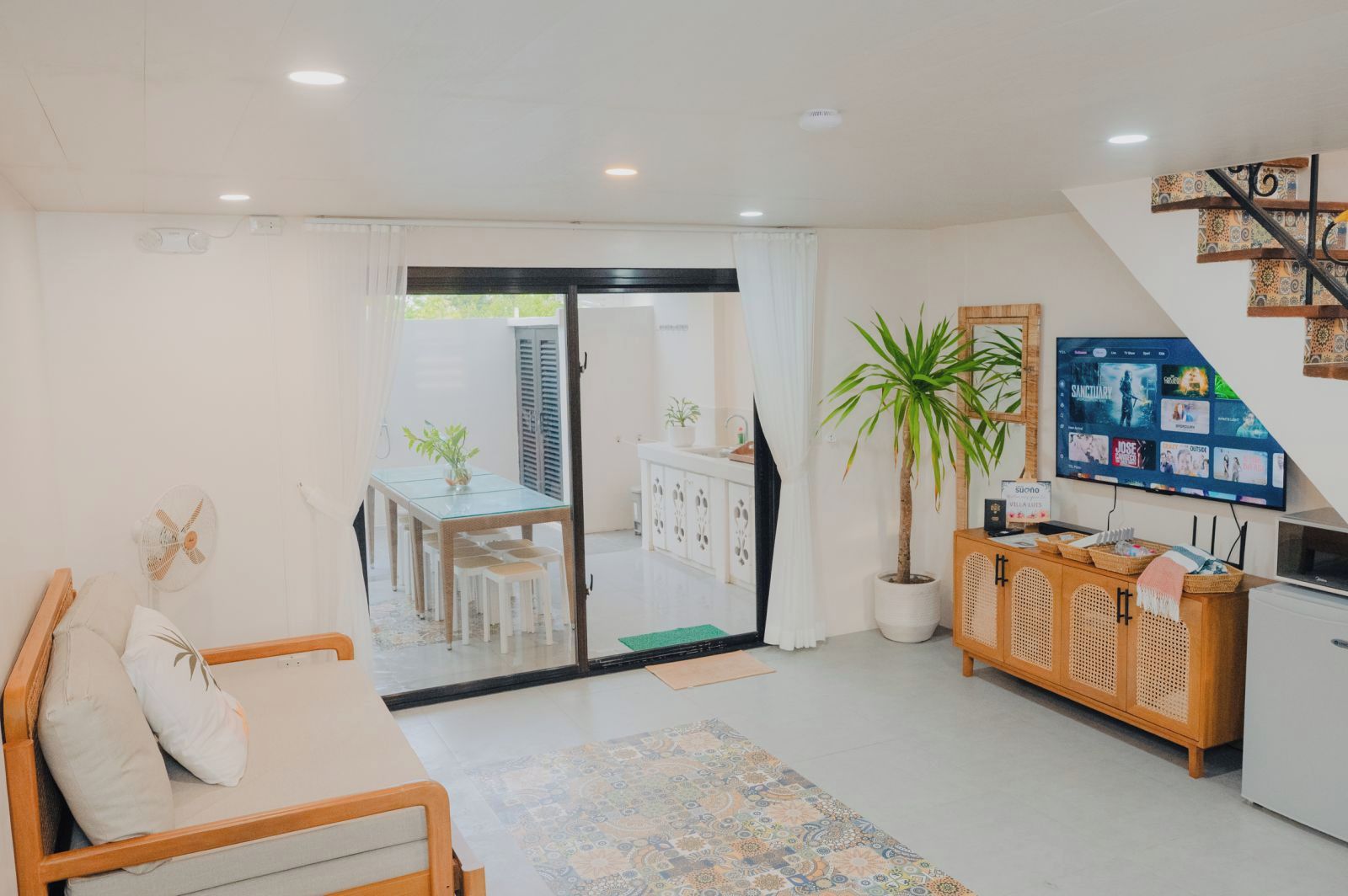 Una sala de estar moderna con un sofá, un comedor con mesa y sillas, un televisor montado en la pared y una escalera que conduce a un nivel superior.