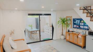 Una sala de estar moderna con un sofá, un comedor con mesa y sillas, un televisor montado en la pared y una escalera que conduce a un nivel superior.