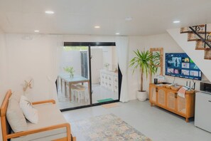 A modern living room with a sofa, a dining area with a table and chairs, a TV mounted on the wall, and a staircase leading to an upper level.