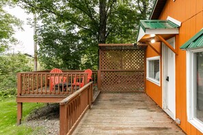 A wooden deck with chairs, a wooden fence, and a building with a window and door.