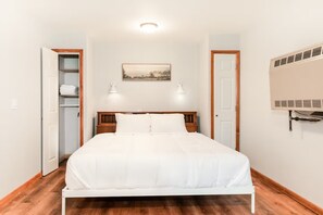 A bedroom with a bed, a nightstand, a wall-mounted heater, and a door leading to a closet.