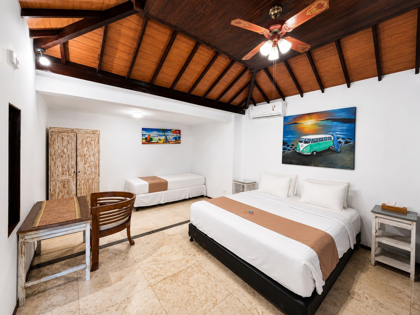 Una habitación de hotel con cama, escritorio, silla, armario y ventilador de techo.