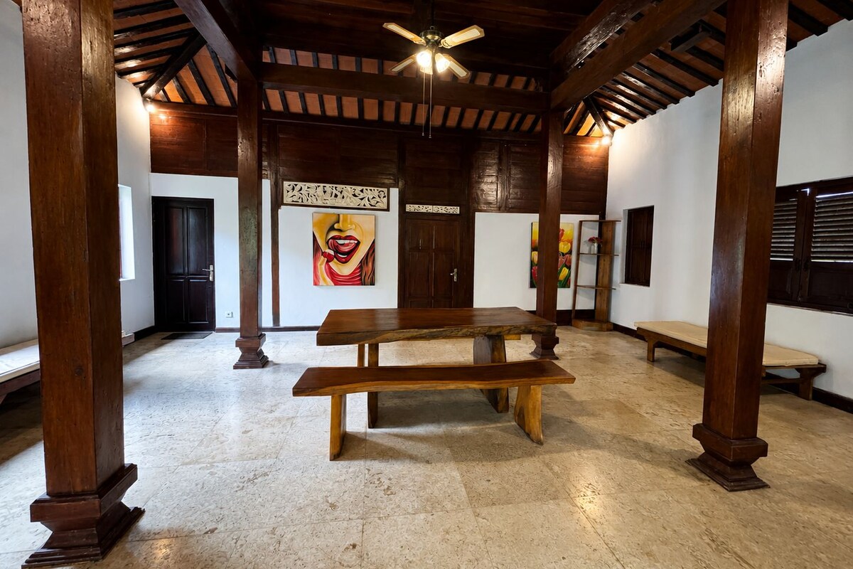Une pièce spacieuse avec un plafond en bois, un ventilateur de plafond, une table en bois et des œuvres d’art accrochées aux murs.