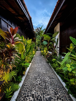 A pathway flanked by lush tropical plants and wooden buildings with a tiled floor. - Surfer Paradise Villas Bali (Pererenan)