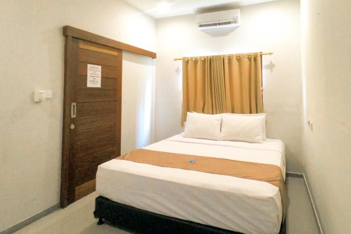 Une petite chambre avec un lit simple, une porte en bois, un ventilateur de plafond et un appareil de climatisation.