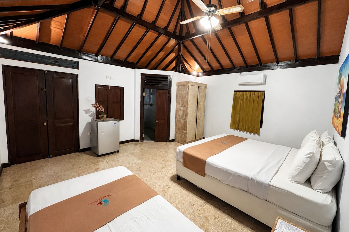 A hotel room with two beds, a ceiling fan, a refrigerator, and a painting on the wall.