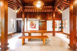Une pièce spacieuse avec un plafond en bois et des colonnes, une grande table en bois et des œuvres d’art accrochées aux murs.