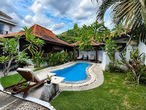 A swimming pool surrounded by lush greenery, a covered seating area, and a stone pathway. - Surfer Paradise Villas Bali (Pererenan)