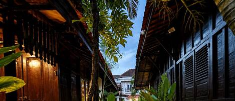 A narrow cobblestone pathway flanked by wooden buildings with traditional architecture, leading to a building with a visible door.
