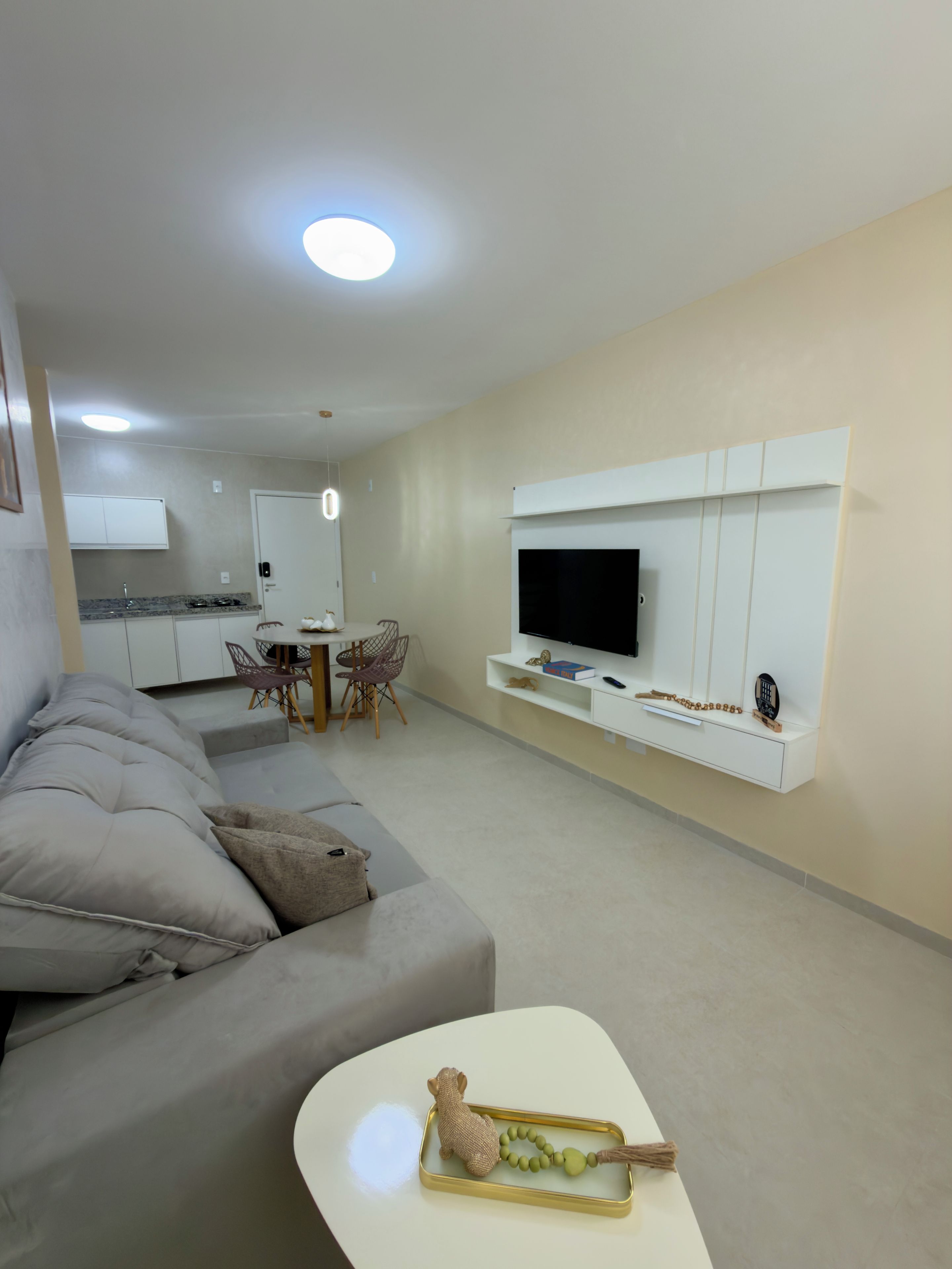 A modern living room with a sofa, a flat-screen TV mounted on a wall, and a dining area with a table and chairs.