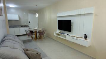 A modern living room with a sofa, a flat-screen TV mounted on a wall, and a dining area with a table and chairs.