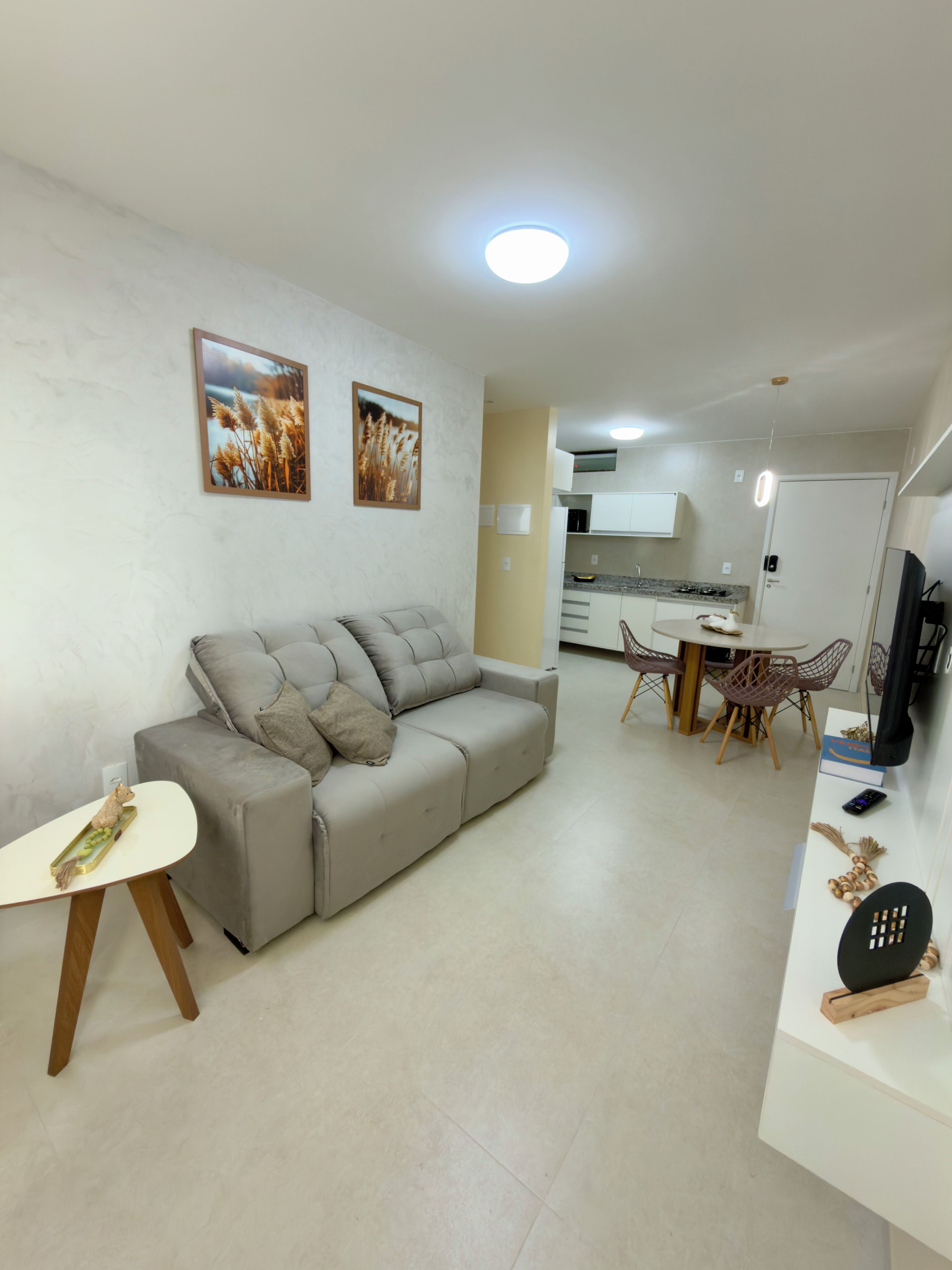 Sala de estar moderna com sofá cinzento, mesa pequena branca e área de jantar com cadeiras e mesa.