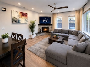 A modern living room with a sectional sofa, a fireplace, a flat-screen TV, and a dining area with a table and chairs. - Mystery Run Retreat | Pool, Spa, Billiards & BBQ (Chico)