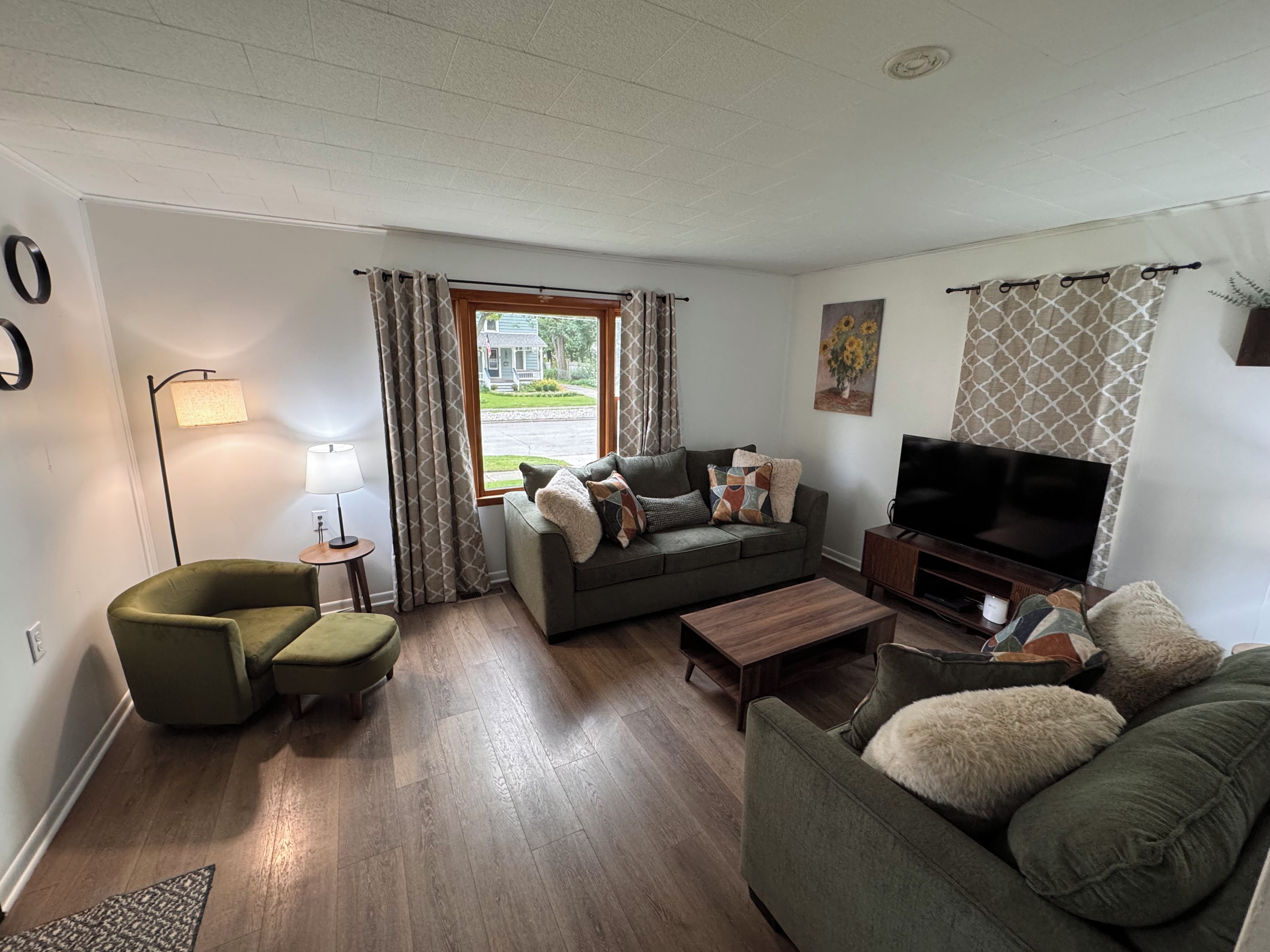 Een woonkamer met een bank, fauteuil, televisie en een lamp.