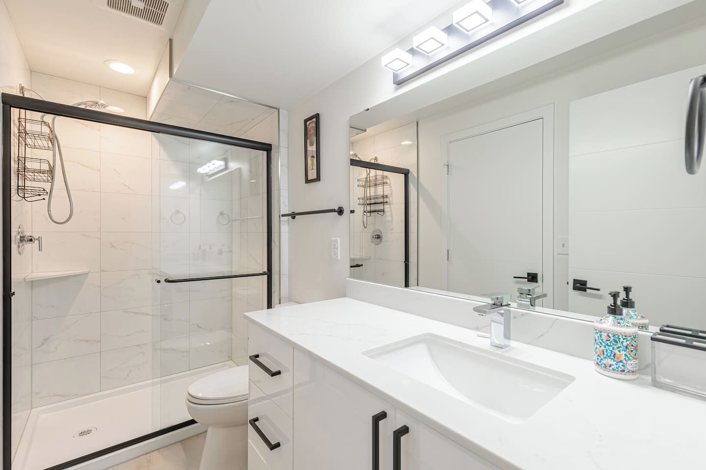 A modern bathroom with a glass shower enclosure, a white toilet, and a large mirror above a white sink with a faucet.