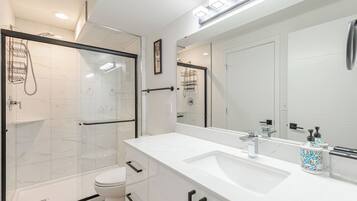 A modern bathroom with a glass shower enclosure, a white toilet, and a large mirror above a white sink with a faucet.
