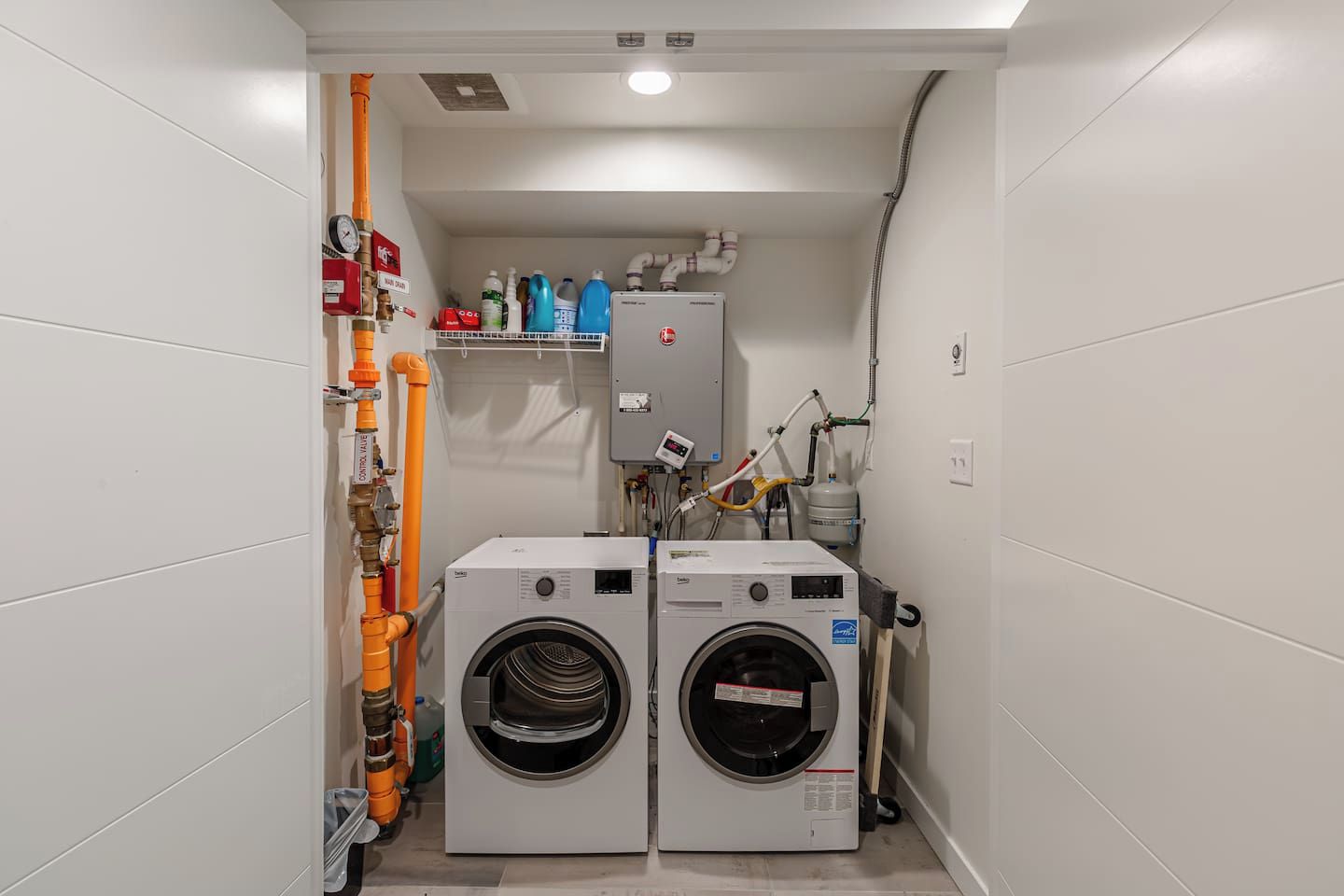 A laundry room with two front-loading washing machines, a control valve, and a water heater.