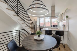 Une cuisine moderne dotée d’un îlot central, d’un coin repas avec une table ronde et des chaises, et d’un escalier avec des rampes noires.