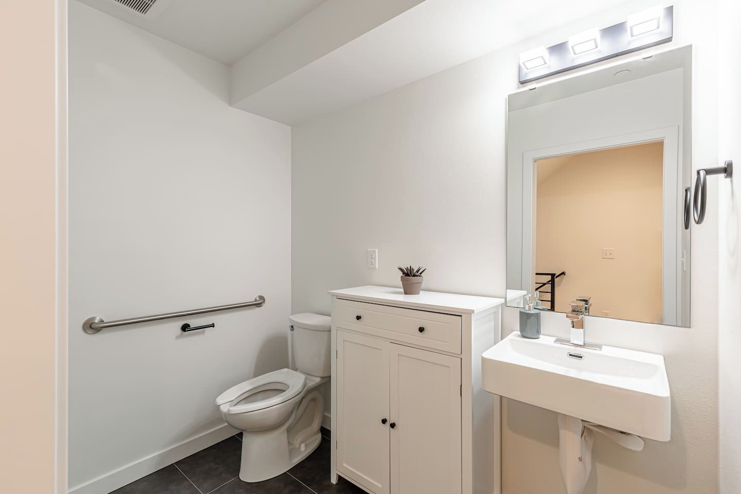 Een badkamer met een toilet, een kastje, een wastafel, een spiegel en een handgreep.