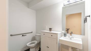 Een badkamer met een toilet, een kastje, een wastafel, een spiegel en een handgreep.