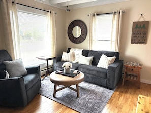 A living room with a grey sofa, a round mirror, and a small wooden side table. - Rev and Ride Trailside Retreat: Direct ATV & Snowmobile Access: Sleeps 9 (Colebrook)