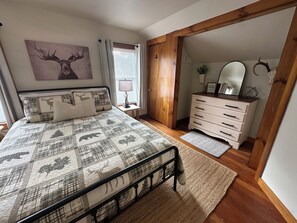 A bedroom with a bed, a dresser, a mirror, a window with curtains, and a painting on the wall. - Rev and Ride Trailside Retreat: Direct ATV & Snowmobile Access: Sleeps 9 (Colebrook)