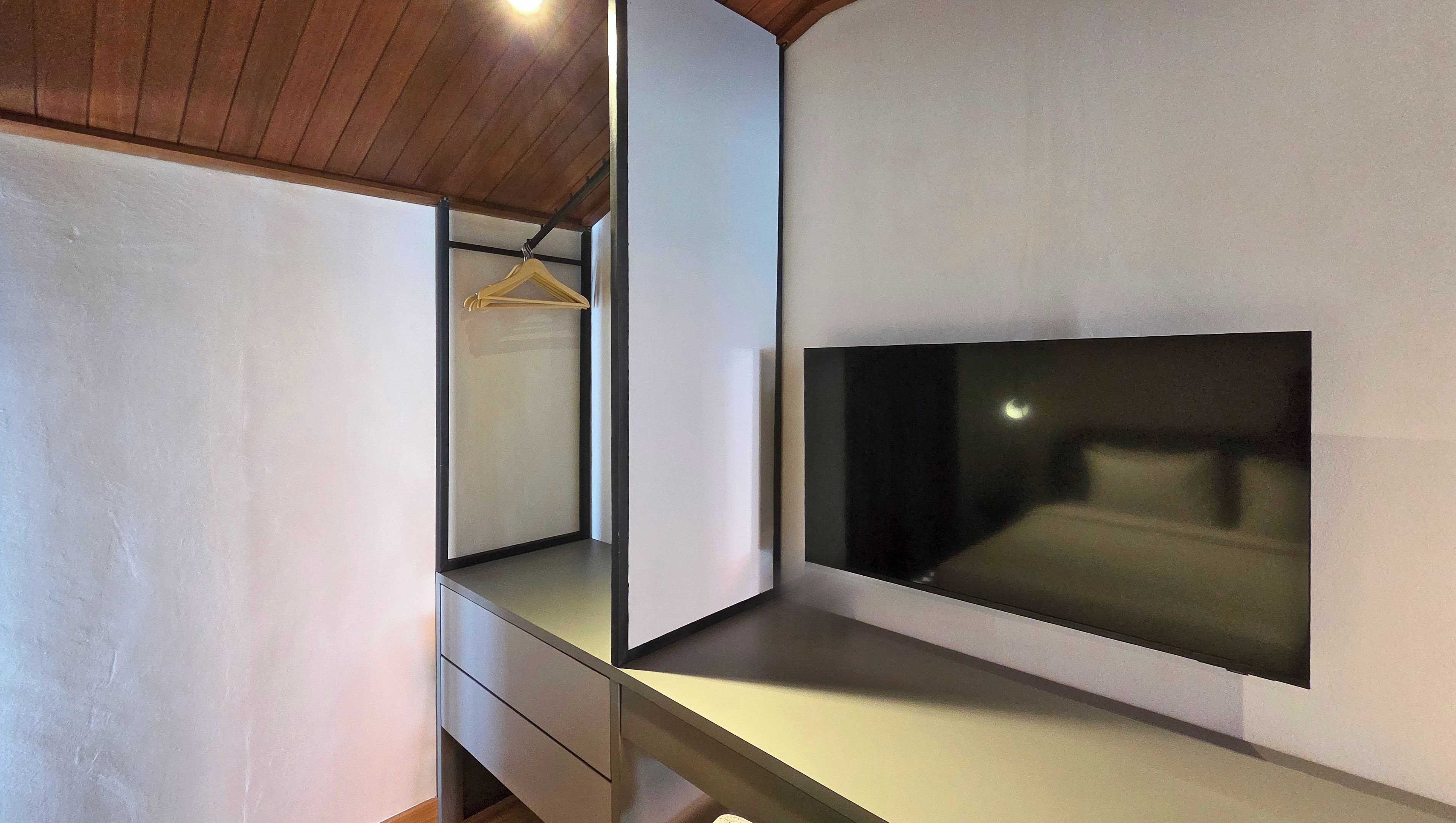 Une chambre à coucher moderne avec un grand téléviseur à écran plat fixé au mur, un plafond en bois et un design minimaliste.