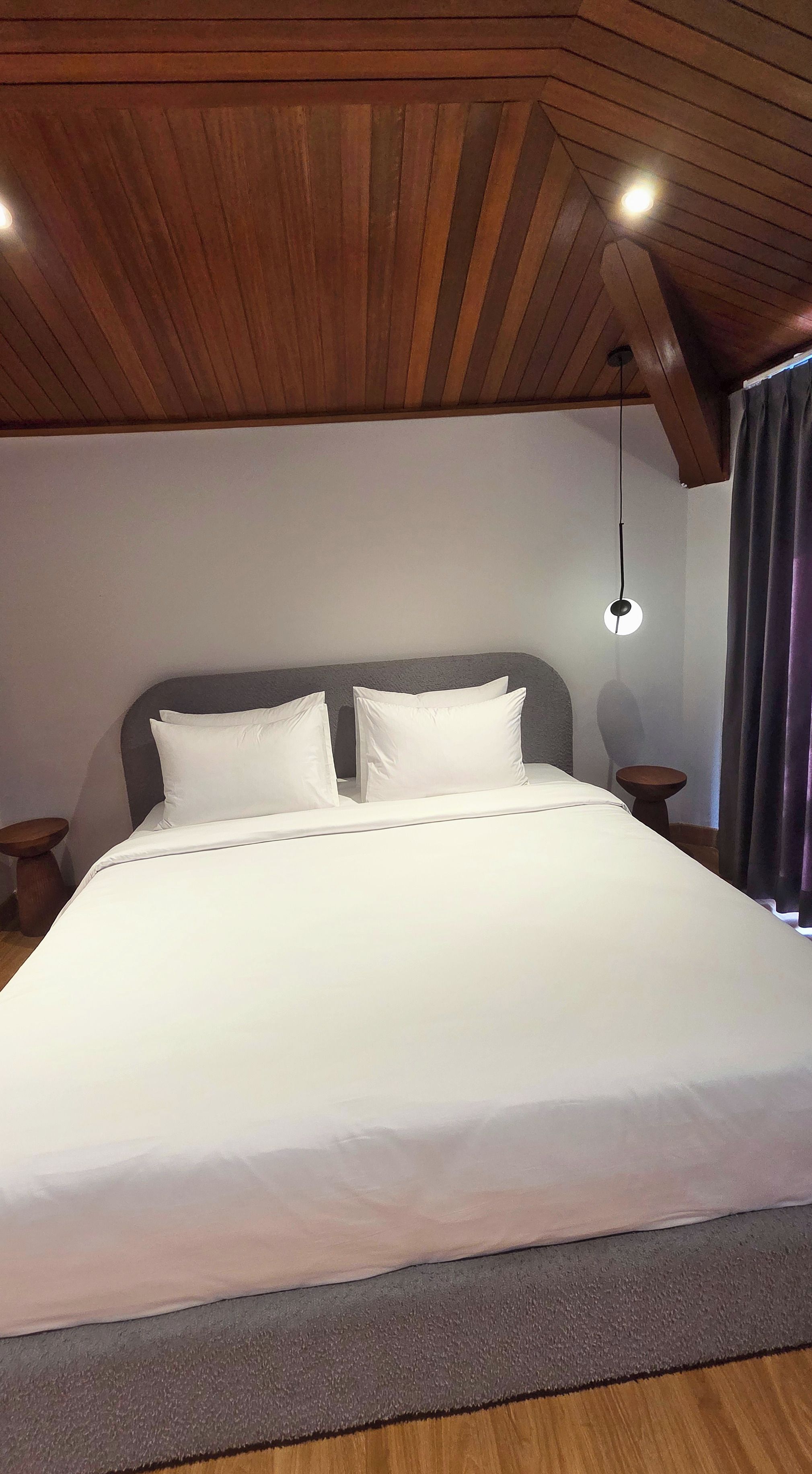 Une chambre à coucher avec un grand lit, un plafond en bois, deux tables de chevet et un luminaire suspendu.