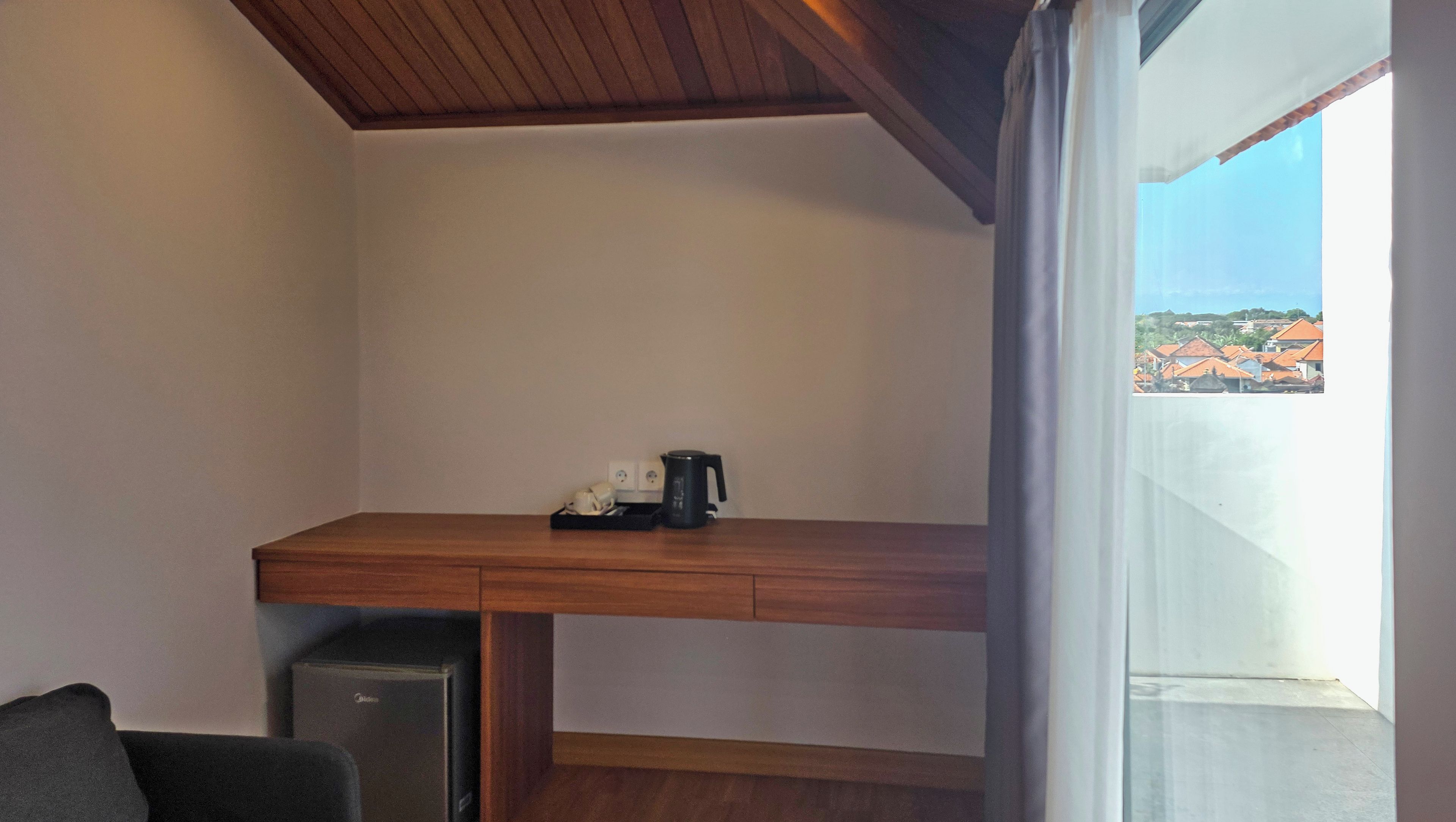 Une petite pièce avec un bureau en bois, une machine à café noire et un petit réfrigérateur.