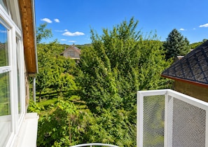 Una propietat residencial amb vista a un paisatge verdós i exuberant, una casa al fons i un balcó blanc amb barana de metall.