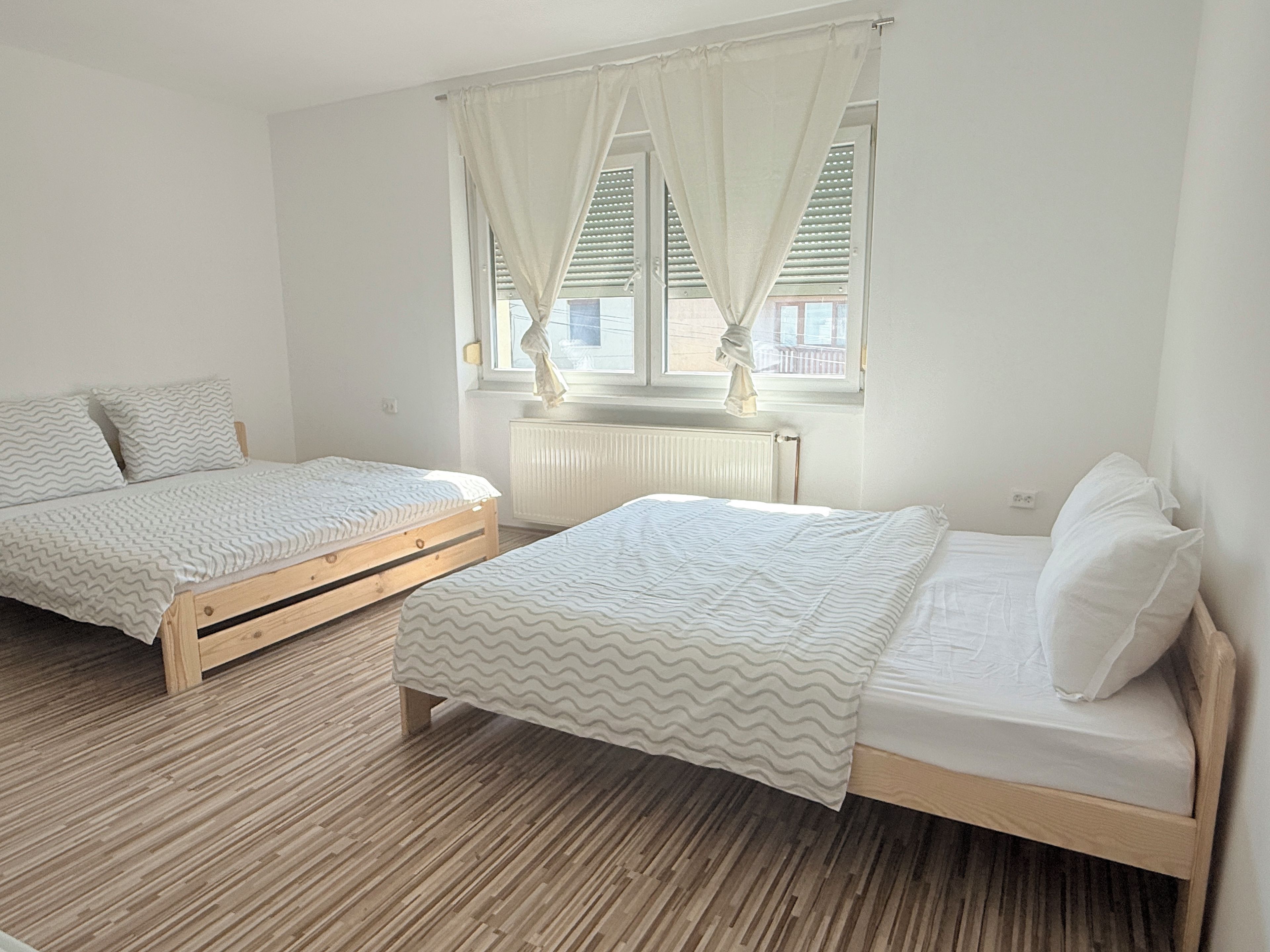 Een slaapkamer met twee houten bedden, een raam met gordijnen en een radiator.