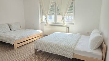 Een slaapkamer met twee houten bedden, een raam met gordijnen en een radiator.