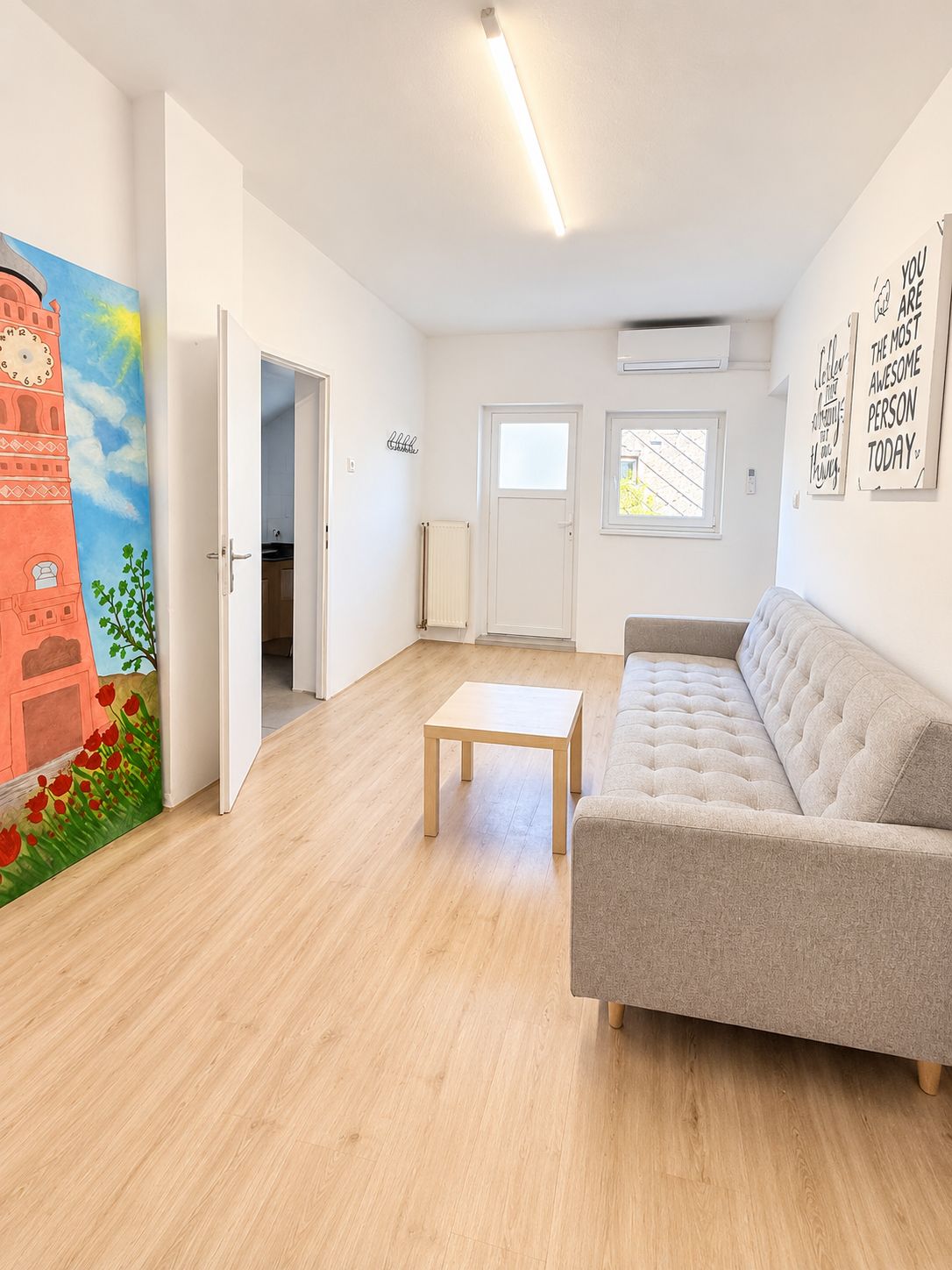 A spacious living room with a sofa, a coffee table, and a door leading to another room.